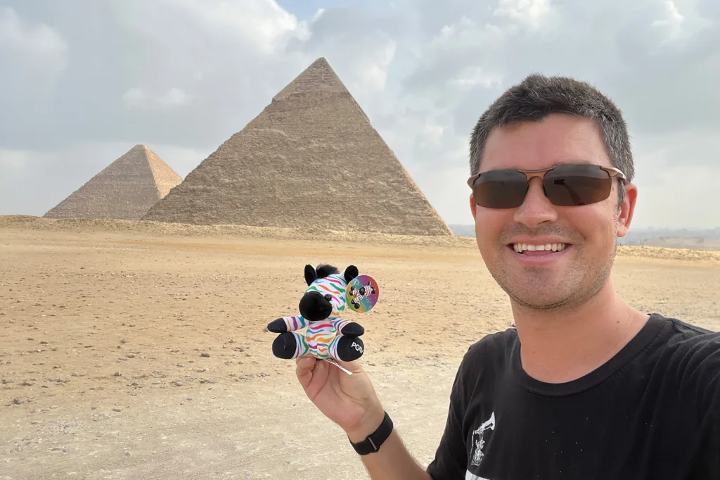 Nick Pelisek holding a zebra-striped Spot plush in front of the Great Pyramids of Giza
