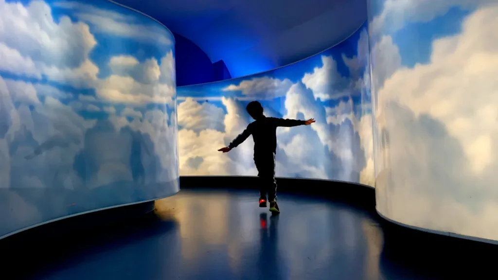Child with arms outstretched like wings walking through a curved cloud-painted gallery at the Air Zoo