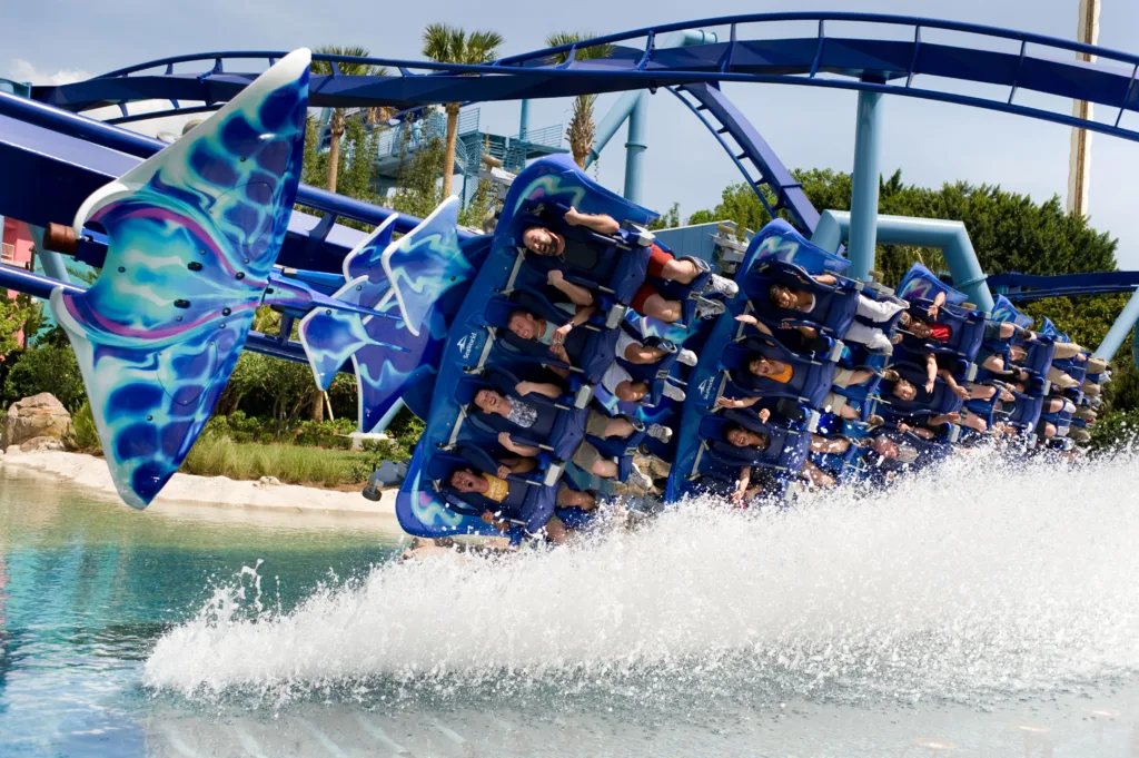 Manta flying roller coaster skimming the water, spraying a wave beside the lagoon at SeaWorld Orlando