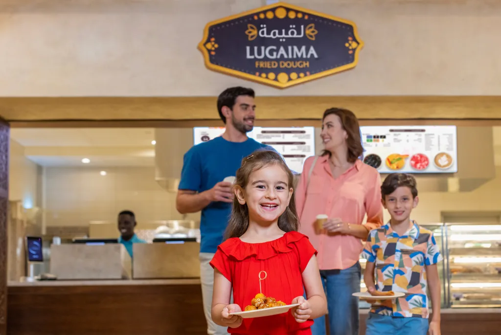 Smiling family with a plate of fried dough at the Lugaima stand at SeaWorld Yas Island, Abu Dhabi