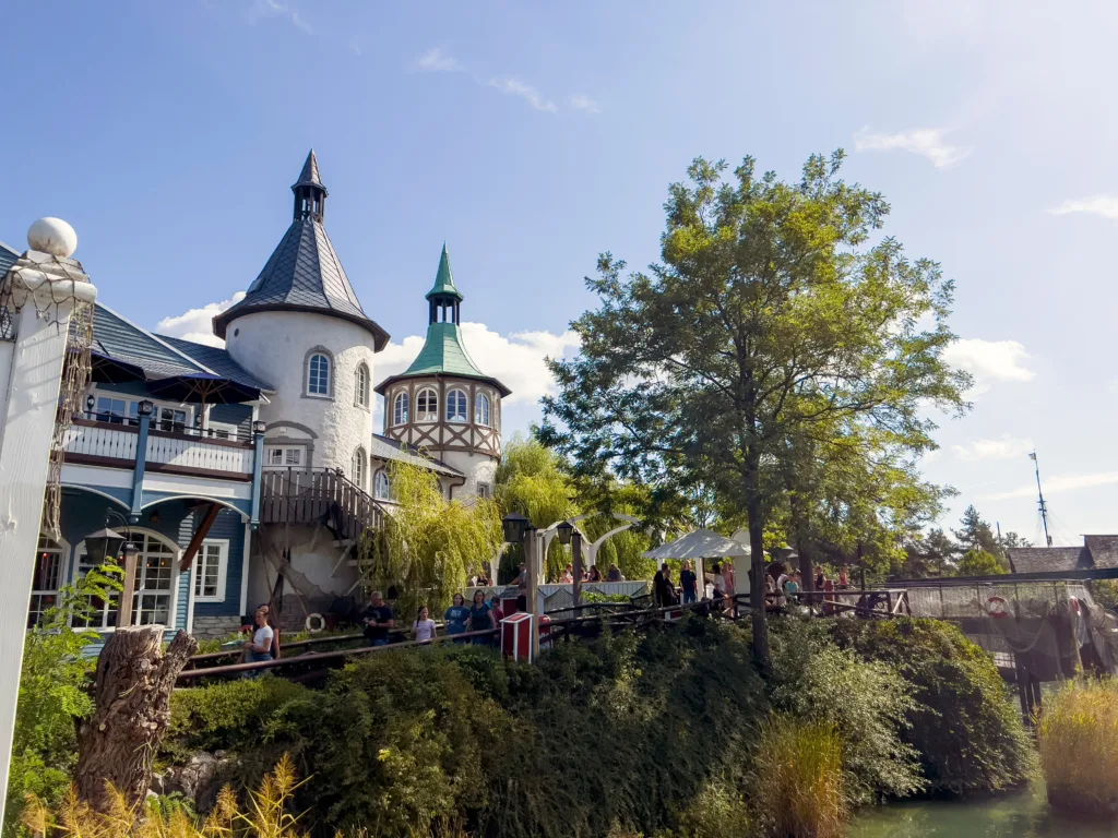 Turreted buildings above a lush waterfront path at Europa-Park, Germany