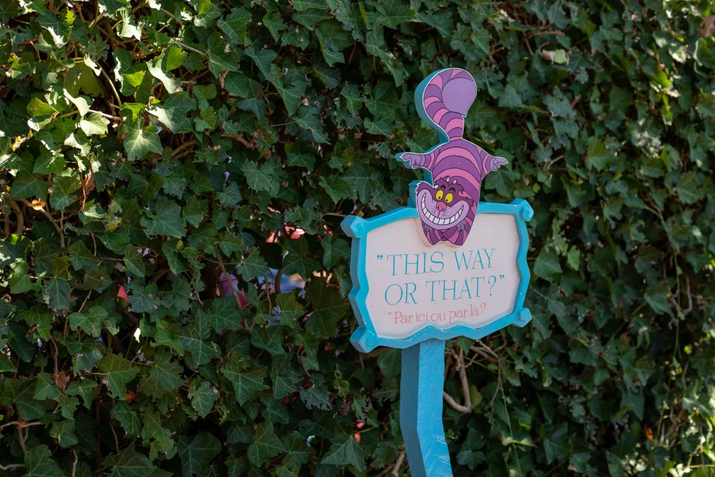 Cheshire Cat sign reading This way or that? against an ivy hedge at Disneyland Paris
