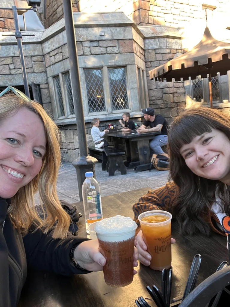Two friends toasting with Butterbeer mugs in a stone courtyard at Universal Orlando Resort
