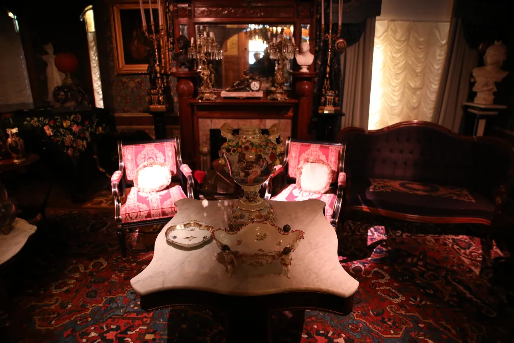 Victorian parlor with pink upholstered chairs, marble table and ornate fireplace in a restored Joplin home