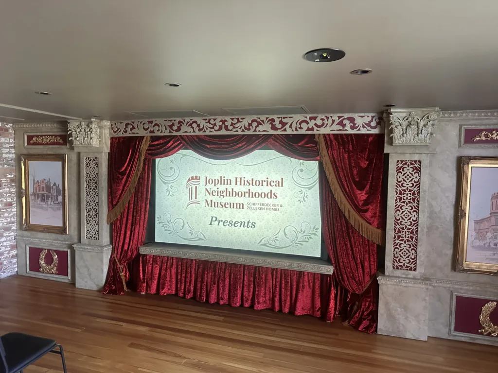 Theater stage with red velvet curtains introducing the Joplin Historical Neighborhoods Museum presentation