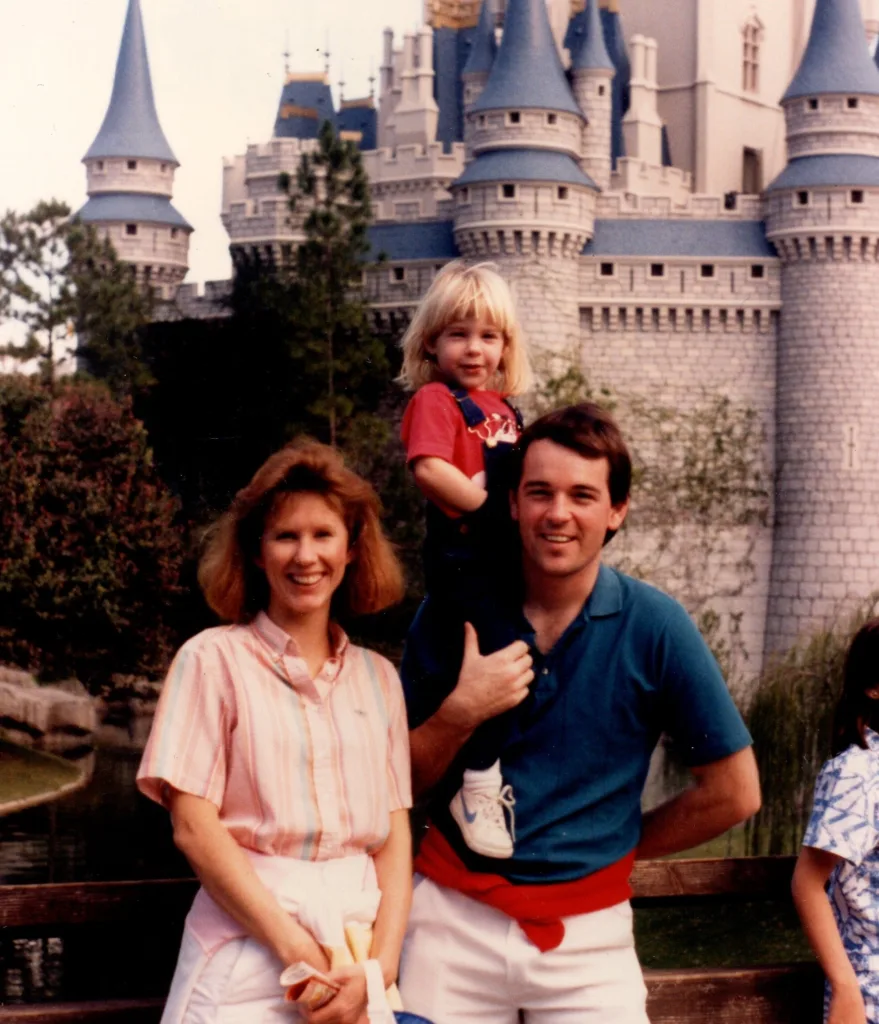 Vintage family photo of a young girl on her father's shoulders beside her mother in front of a fairy-tale castle